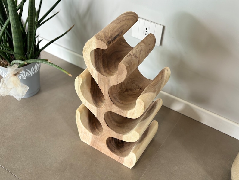 May include: A wooden wine rack with a unique, organic design. The rack is made of natural wood and has a light brown color. It features multiple curved shelves that can hold up to 6 bottles of wine.
