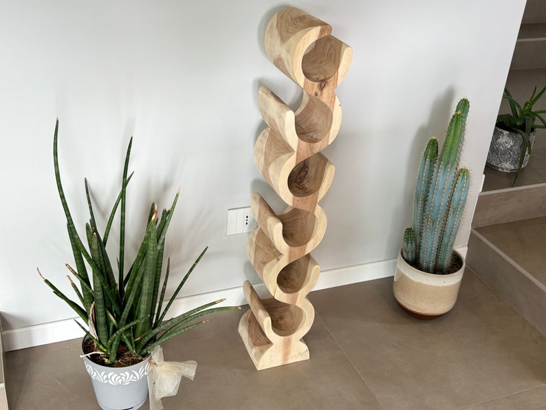 May include: A wooden wine rack with a unique, curved design. The rack is made of light-colored wood and features six individual slots for wine bottles. The rack is free-standing and has a natural, organic aesthetic, perfect for home decor.