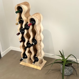 May include: A wooden wine rack with a wavy design, holding multiple bottles of wine. The rack is made of light brown wood and has a natural finish. The rack is standing on a light brown floor.
