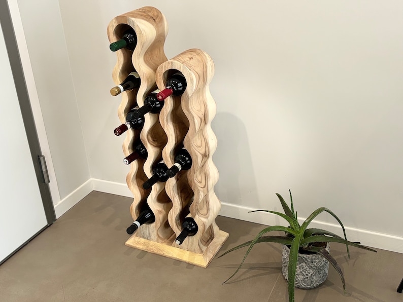 May include: A wooden wine rack with a wavy design, holding multiple bottles of wine. The rack is made of light brown wood and has a natural finish. The rack is standing on a light brown floor.