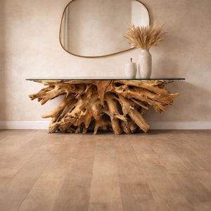 Pode incluir: Uma consola única com um tampo de vidro transparente suportado por uma base de madeira natural esculpida de forma intrincada. A mesa está colocada contra uma parede neutra com um espelho oval com moldura dourada e vasos decorativos. A base de madeira tem cerca de 152 cm de comprimento.