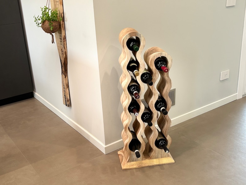 May include: A wooden wine rack with a wavy design holds multiple bottles of wine. The rack is made of light brown wood and has a natural finish. The bottles are arranged in a staggered pattern, with the tops of the bottles visible.