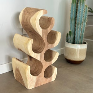 May include: A wooden wine rack shaped like a tree with six bottle holders. The rack is made of light brown wood and has a natural finish.