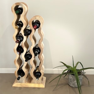 May include: A wooden wine rack with a wavy design holds multiple bottles of wine. The rack is made of light brown wood and has a natural finish. The rack is standing on a light brown tile floor.