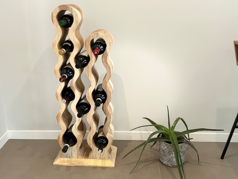 May include: A wooden wine rack with a wavy design holds multiple bottles of wine. The rack is made of light brown wood and has a natural finish. The rack is standing on a light brown tile floor.