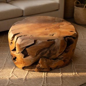 Pode incluir: Uma mesa de centro redonda de madeira natural com uma superfície áspera e texturizada. A mesa é de cor castanho quente e tem uma forma única e orgânica. A mesa tem aproximadamente 76 cm de diâmetro.