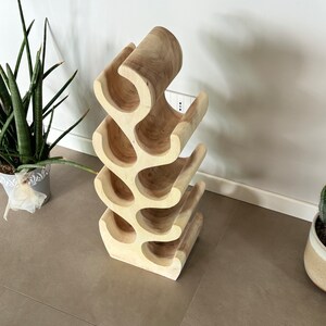 May include: A wooden wine rack shaped like a tree branch with six bottle holders. The rack is made of light brown wood and has a natural finish.