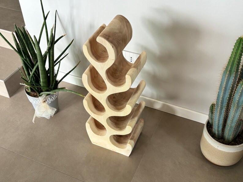May include: A wooden wine rack shaped like a tree branch with six bottle holders. The rack is made of light brown wood and has a natural finish.