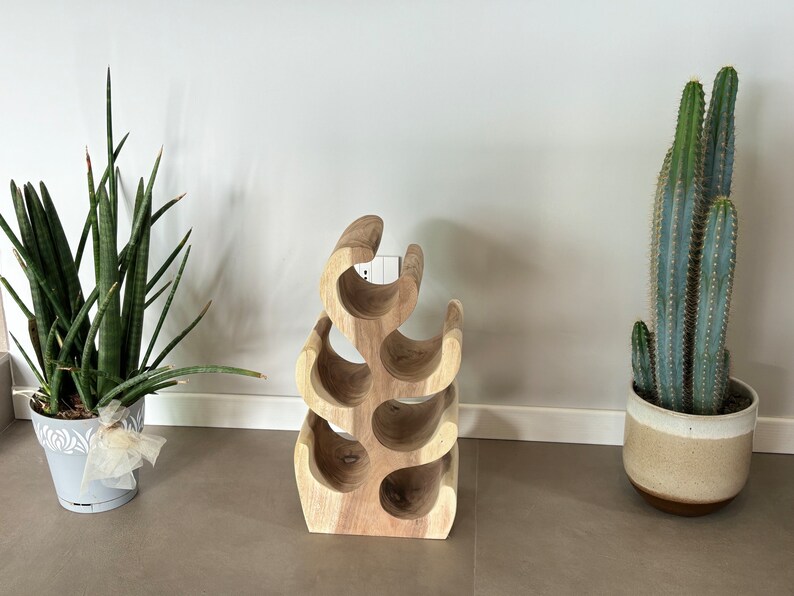 May include: A wooden wine rack shaped like a tree with six bottle holders. The rack is made of light brown wood and has a natural finish. The rack is sitting on a light brown floor.