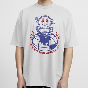 May include: A gray t-shirt with a blue and red graphic of a cartoon character standing on a globe. The text "Stack it High Watch it Fly" is printed below the graphic.