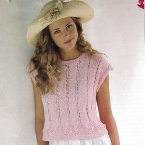 May include: A woman wearing a light pink knitted top and a straw hat with a decorative accent. The top has a textured design and is paired with a white skirt. The words "DOUBLE KNITTING" are in the top left corner.