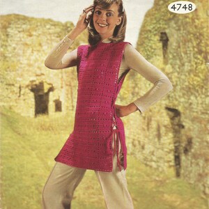 May include: A pink crochet top with a tie at the side. The top is sleeveless and has a round neckline. The model is wearing the top with white pants and is standing in front of a stone wall.
