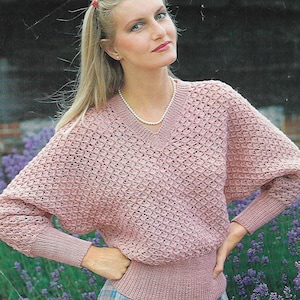 May include: A pink knitted sweater with a v-neck and a textured pattern. The sweater has long sleeves and a fitted waist.