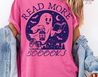 May include: Pink t-shirt with a navy blue graphic featuring a friendly ghost holding a lantern and a book, with the words "READ MORE BOOKS" in a circular design. The shirt has rolled-up sleeves.