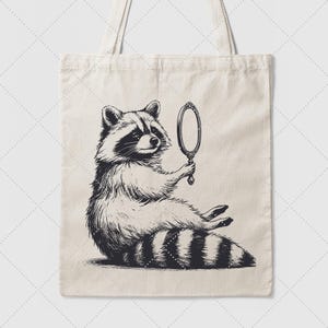 K&ouml;nnte beinhalten: Eine Schwarzwei&szlig;illustration eines Waschb&auml;ren, der einen Handspiegel h&auml;lt. Der Waschb&auml;r sitzt auf seinen Hinterbeinen und schaut in den Spiegel. Die Illustration befindet sich auf einer wei&szlig;en Tragetasche.