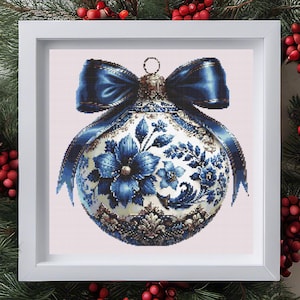 Può includere: Ornamento natalizio incorniciato con un design floreale blu e bianco. L'ornamento sferico ha un fiocco di nastro blu. La cornice è bianca e lo sfondo è rosa chiaro.
