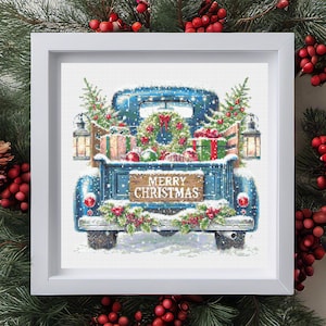 Puede incluir: Un bordado enmarcado que representa una camioneta azul vintage llena de decoraciones navideñas. La caja de la camioneta contiene regalos envueltos, una corona y pequeños árboles de Navidad. Un letrero de madera en el portón trasero dice "MERRY CHRISTMAS". La nieve cubre la escena.