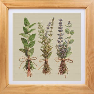 Può includere: Opera d'arte a punto croce di tre mazzi di erbe, ciascuno legato con spago. Le erbe includono menta verde, rosmarino e lavanda, con cuciture dettagliate e uno sfondo neutro. L'opera è incorniciata in una cornice di legno chiaro.