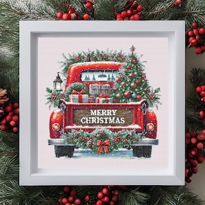 May include: A framed cross-stitch featuring a red vintage truck decorated for Christmas. The truck bed is filled with gifts, a Christmas tree, and greenery. The words "MERRY CHRISTMAS" are displayed on the truck's tailgate. The frame is white.