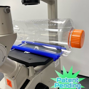 May include: A white microscope with a blue platform and a clear plastic bottle with an orange lid. The microscope has a black knob and a "Patent Pending" sign in the lower right corner.