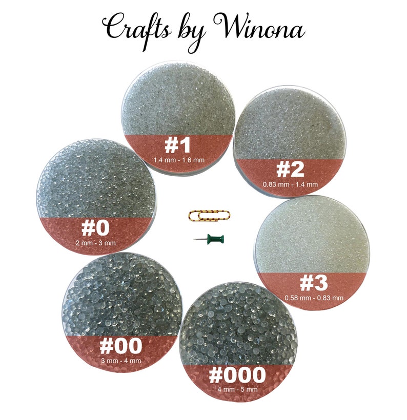 Op de afbeelding: Zes doorzichtige glazen potten gevuld met verschillende maten glazen kralen. De potten zijn gelabeld met de nummers 0, 00, 1, 2, 3 en 000. Elke pot heeft een label met de overeenkomstige maat van de kralen in millimeters.