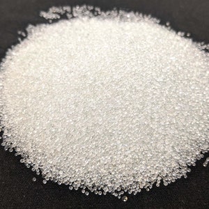 May include: A close-up of a pile of small, clear glass beads. The beads are round and smooth, and they are scattered on a black surface.