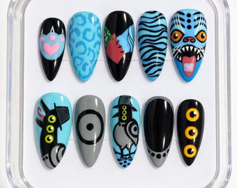 May include: A set of ten almond-shaped press-on nails in a clear plastic case. The designs feature black, blue, gray, and yellow colors with motifs including a pink heart, animal prints, a monster face, a bird, and multiple yellow eyes.