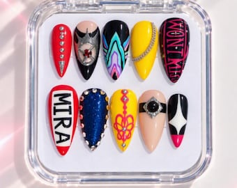 Pode incluir: Um conjunto de dez unhas postiças em formato amêndoa num estojo transparente. Os designs incluem vermelho com strass, preto com detalhes prateados, padrões multicoloridos, amarelo com uma corrente e preto com o texto WONT KISS. Outros apresentam o texto MIRA, glitter azul, amarelo com linhas cor-de-rosa, nude com uma gema preta e uma estrela preta e branca.