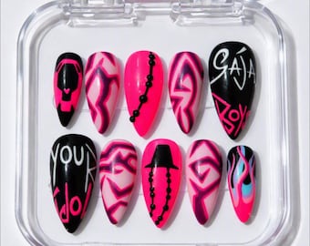 May include: A set of ten press-on nails in a clear plastic case. The nails feature a vibrant color palette of hot pink, black, and white. Designs include abstract lightning patterns, black beaded lines, a black hat icon, and text reading "GAJA" and "YOUR IDOL".