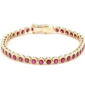 Puede incluir: Un brazalete de oro con una fila de piedras redondas de rubí rojo.