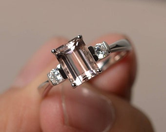 May include: A silver ring featuring a large, rectangular, pale pink gemstone and two smaller, round, clear gemstones set into the band.