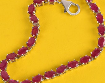 May include: A silver bracelet with a clasp closure, featuring a row of oval-shaped ruby red gemstones.