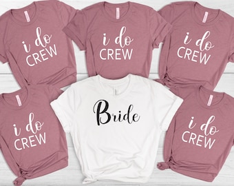 Peut inclure: Cinq t-shirts avec le texte "i do crew" en blanc sur un fond mauve. Un t-shirt blanc avec le texte "Bride" en noir.