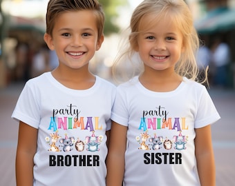 May include: Two children wearing white t-shirts with a party animal design. The boy's shirt says "party animal brother" and the girl's shirt says "party animal sister".