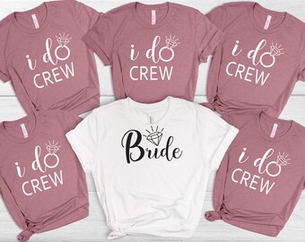 Peut inclure: Cinq t-shirts sur le thème d'une fête de mariage. Quatre des t-shirts sont de couleur rose poussiéreux avec le texte "i do crew" et un graphique de bague de diamant. Un t-shirt est blanc avec le texte "Bride" et un graphique de bague de diamant.
