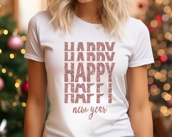 May include: White t-shirt with a glittery pink design. The design includes the word "HAPPY" in large letters, repeated above and below, with "new year" written in cursive at the bottom. The shirt is short-sleeved.