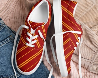 May include: A pair of white canvas low-top sneakers with red and gold striped pattern. The shoes are on a pink and blue fabric background.