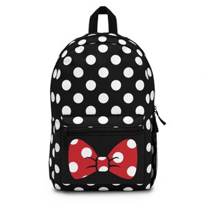 May include: Black backpack with white polka dots and a red bow design on the front pocket. The backpack has a top handle, a front zippered pocket, and side mesh pockets. The bow is red with white polka dots.