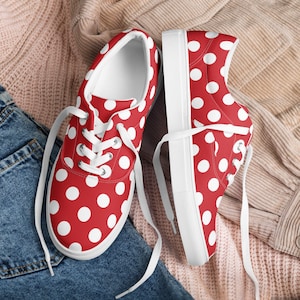 Puede incluir: Un par de zapatillas de lona rojas con lunares blancos. Las zapatillas tienen cordones blancos y suelas blancas.