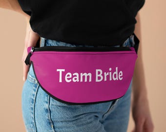 May include: A pink fanny pack with a black zipper and a white inscription that reads "Team Bride".