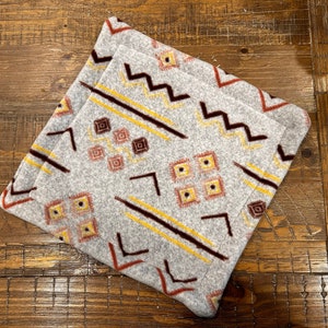 May include: A gray throw pillow with a geometric pattern in shades of brown, yellow, and red. The pattern features zigzags, squares, and lines.
