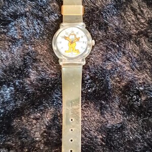 May include: A clear plastic watch with a white face featuring a cartoon image of Garfield. The watch has a clear plastic band with a silver buckle.
