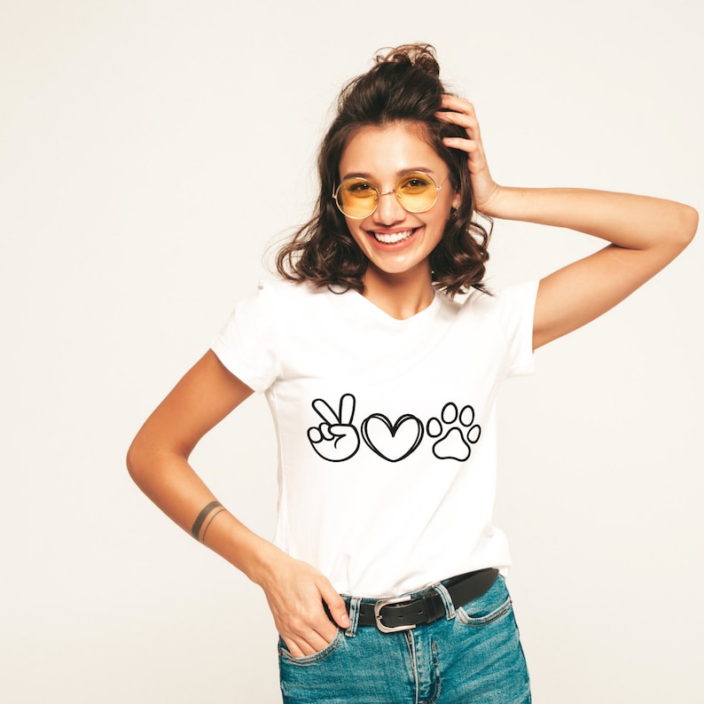 May include: White t-shirt with a black graphic featuring a peace sign, a heart, and a paw print. The shirt is made of a soft material and is suitable for casual wear. The design is simple and bold, perfect for pet lovers.