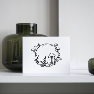 May include: A black and white illustration of a moon with mushrooms growing around it. The moon has a dotted pattern and stars around it.