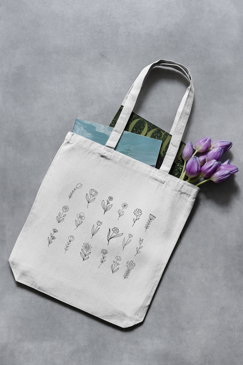 May include: A white canvas tote bag with black line drawings of flowers. The bag is filled with a magazine and a bouquet of purple tulips.