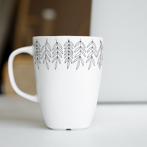 May include: White ceramic mug with a black line drawing of leaves around the top edge.