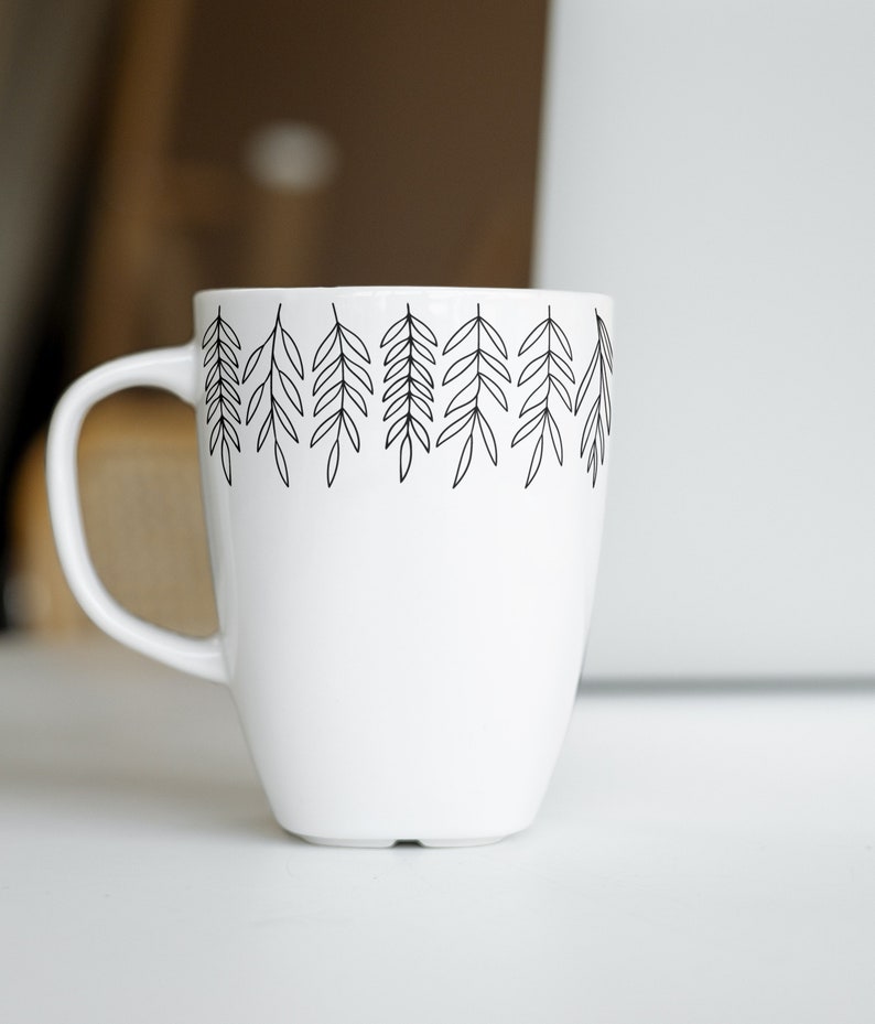 May include: White ceramic mug with a black line drawing of leaves around the top edge.