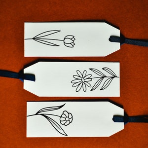 May include: Three white gift tags with black ink drawings of flowers. Each tag has a black ribbon attached.