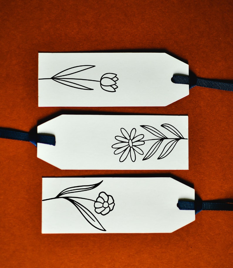 May include: Three white gift tags with black ink drawings of flowers. Each tag has a black ribbon attached.