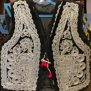 May include: A black vest with silver embroidery and mirrored accents. The vest has a traditional design with intricate details.